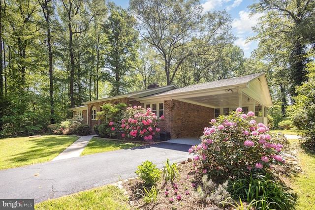 view of property exterior with a chimney, a lawn, a carport, brick siding, and aphalt driveway