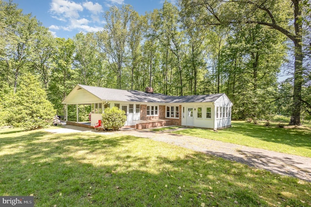 rear view of house featuring brick siding, driveway, a yard, and a chimney