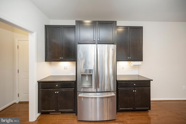 kitchen with dark stone counters, decorative backsplash, wood finished floors, and stainless steel fridge with ice dispenser