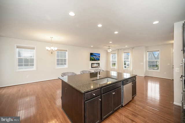 kitchen featuring stainless steel dishwasher, dark brown cabinets, open floor plan, a sink, and dark stone countertops