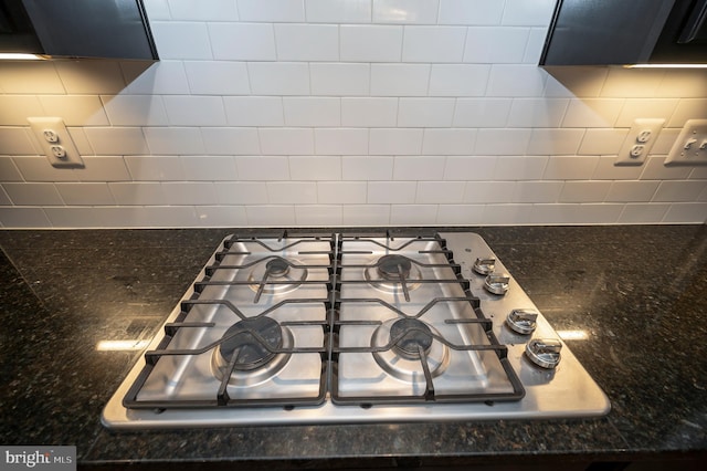 details with stainless steel gas stovetop, dark stone counters, and backsplash