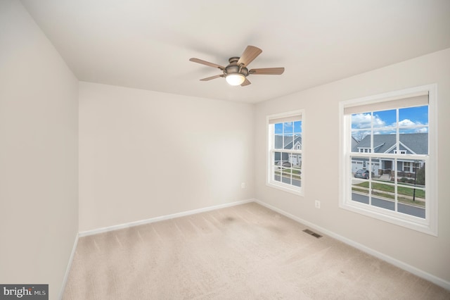 spare room with baseboards, a ceiling fan, light colored carpet, and visible vents