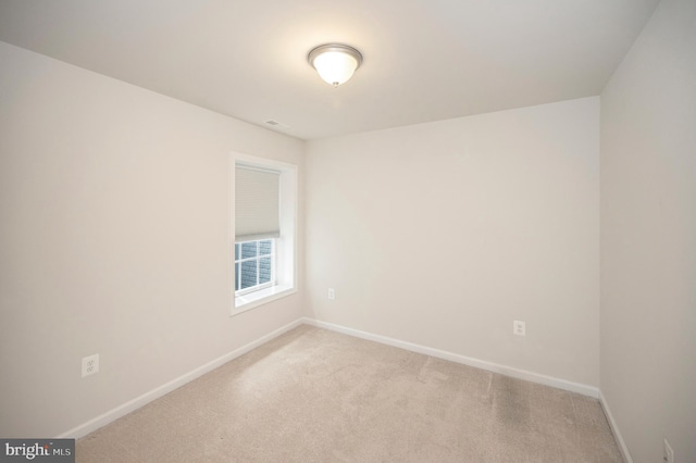 spare room featuring light colored carpet and baseboards