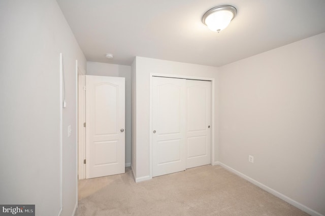 unfurnished bedroom featuring baseboards, light carpet, and a closet