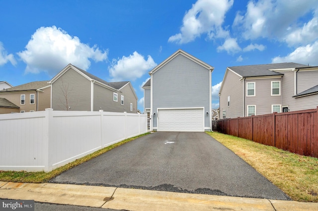 view of side of home featuring a garage, fence, driveway, and a residential view