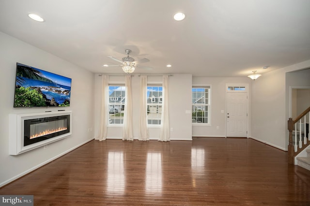 unfurnished living room with a glass covered fireplace, stairs, recessed lighting, a ceiling fan, and wood finished floors