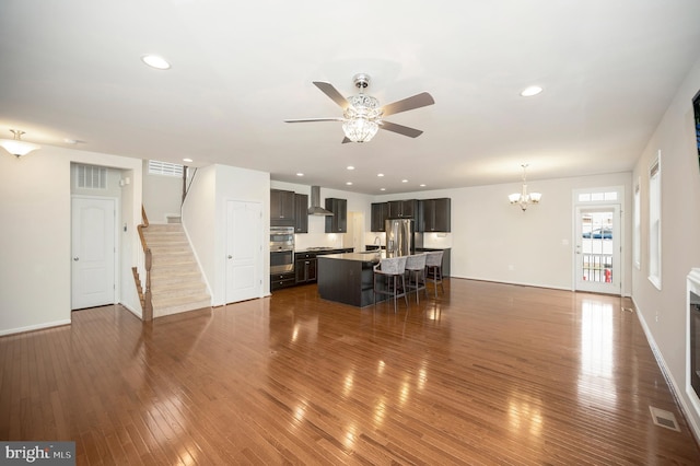 living room with dark wood-style flooring, stairs, baseboards, ceiling fan with notable chandelier, and recessed lighting