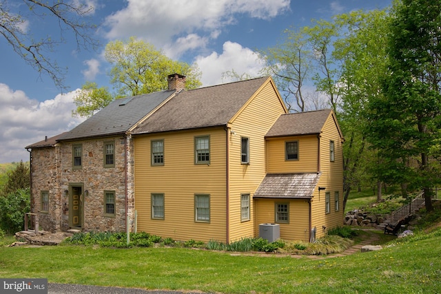 back of property featuring a lawn, central AC unit, and a chimney