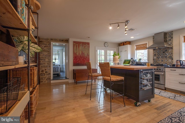 kitchen featuring high end stainless steel range oven, light wood-type flooring, white cabinets, wood counters, and wall chimney exhaust hood