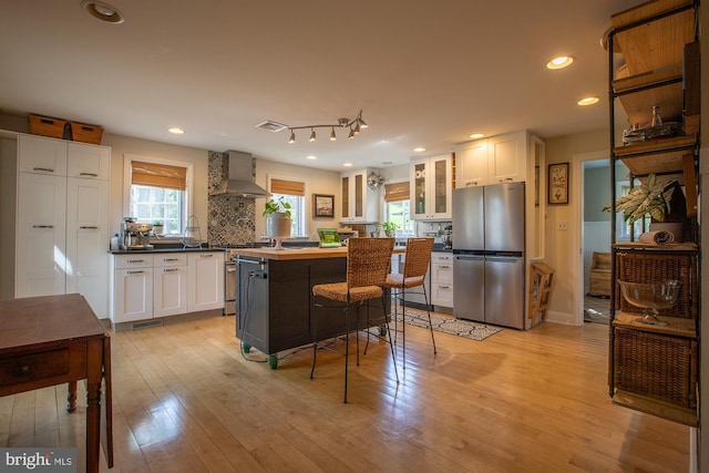 kitchen with a kitchen island, glass insert cabinets, wall chimney range hood, white cabinetry, and stainless steel appliances