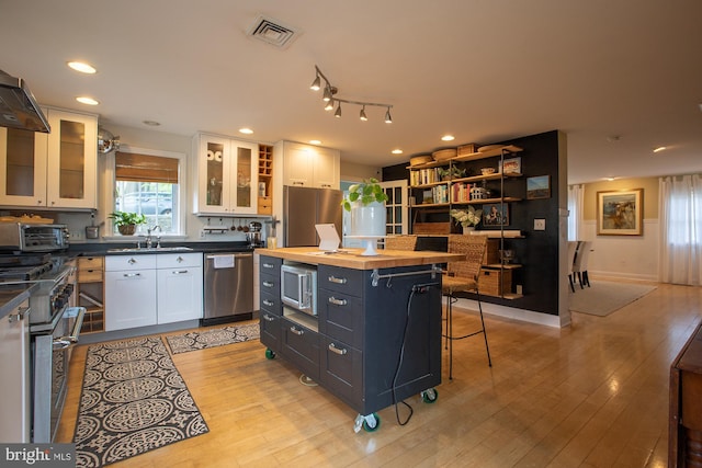 kitchen with appliances with stainless steel finishes, a sink, wood counters, white cabinetry, and visible vents