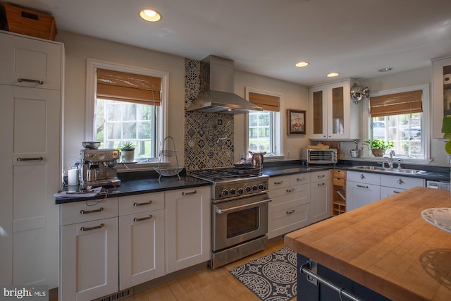 kitchen featuring a sink, high end stainless steel range oven, butcher block countertops, wall chimney exhaust hood, and glass insert cabinets