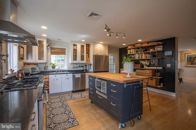 kitchen with wall chimney range hood, visible vents, a sink, wood counters, and stainless steel appliances