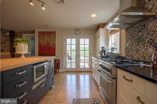 kitchen featuring french doors, wall chimney exhaust hood, stainless steel appliances, white cabinetry, and light wood-type flooring