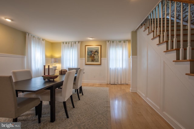 dining room with stairway, a wainscoted wall, a decorative wall, and light wood-style flooring
