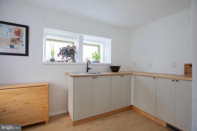 kitchen with white cabinets, visible vents, a sink, and light wood finished floors
