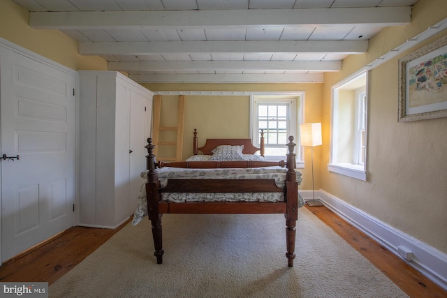 bedroom with baseboards, wood finished floors, and beamed ceiling