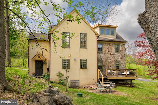 rear view of property featuring a lawn, stucco siding, stone siding, and a deck