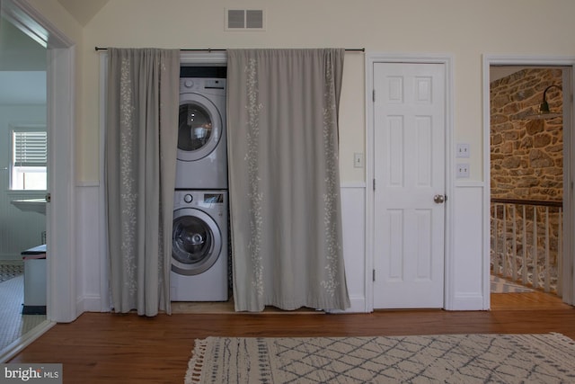 laundry room with laundry area, stacked washer / drying machine, visible vents, and wood finished floors