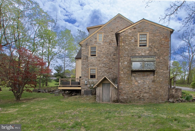 rear view of house with a lawn, central AC, a wooden deck, and stone siding