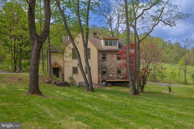 back of property featuring a lawn, a wooden deck, a chimney, and stucco siding