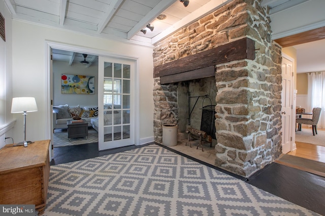 interior space featuring ceiling fan, a stone fireplace, wainscoting, beam ceiling, and wood finished floors