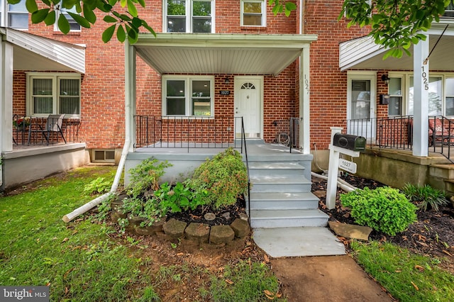 view of exterior entry featuring a porch and brick siding
