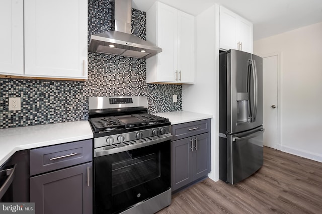 kitchen featuring appliances with stainless steel finishes, wall chimney exhaust hood, wood finished floors, light countertops, and white cabinetry