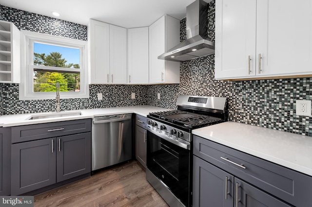 kitchen with appliances with stainless steel finishes, wall chimney range hood, a sink, and gray cabinets