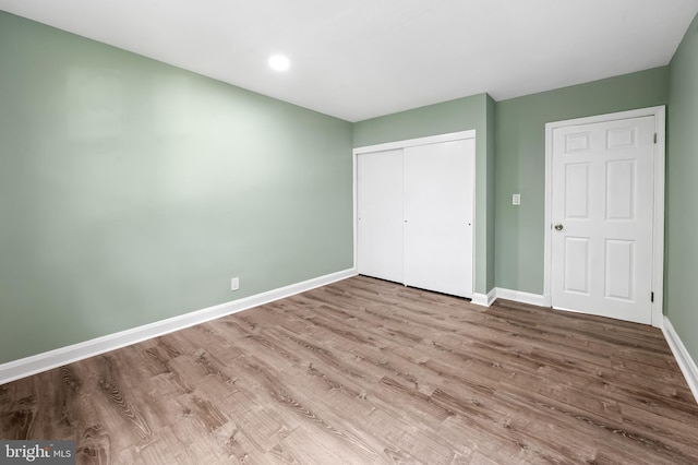 unfurnished bedroom featuring baseboards, wood finished floors, a closet, and recessed lighting