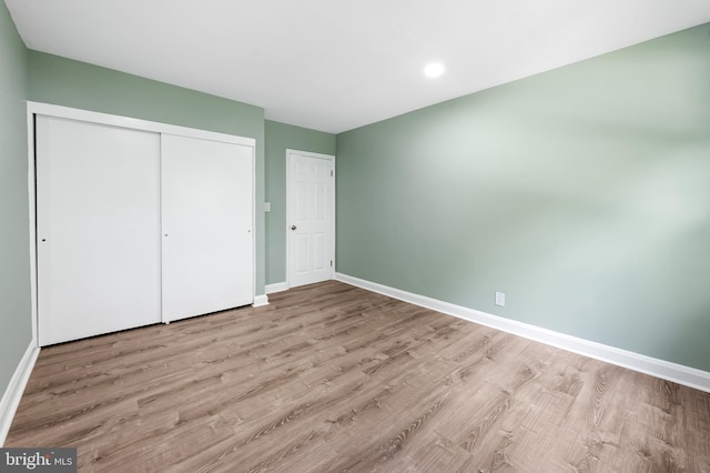 unfurnished bedroom featuring wood finished floors, baseboards, a closet, and recessed lighting