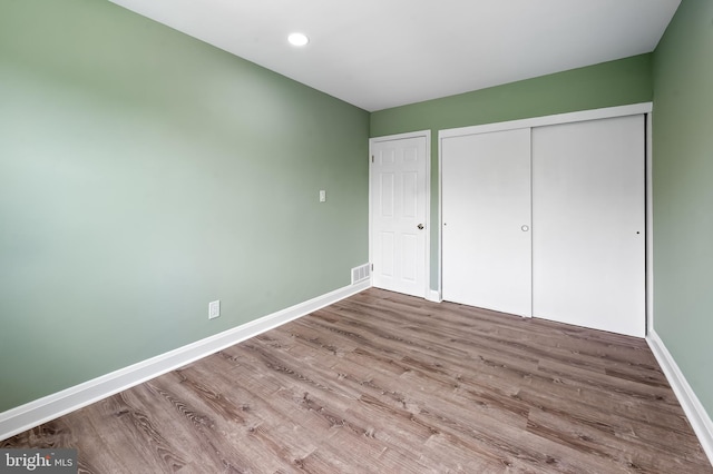 unfurnished bedroom featuring baseboards, wood finished floors, a closet, and recessed lighting