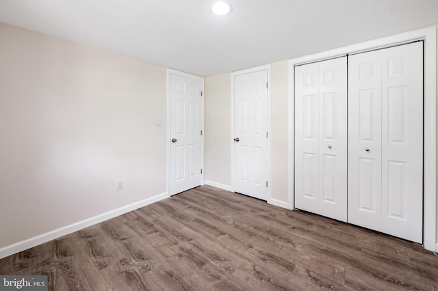 unfurnished bedroom with wood finished floors, baseboards, a closet, and recessed lighting