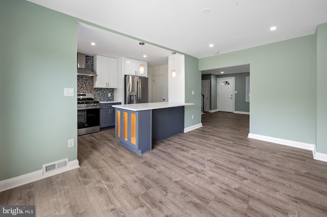 kitchen with appliances with stainless steel finishes, wall chimney exhaust hood, light countertops, baseboards, and tasteful backsplash