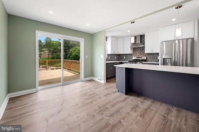 kitchen with appliances with stainless steel finishes, wall chimney range hood, backsplash, light countertops, and baseboards