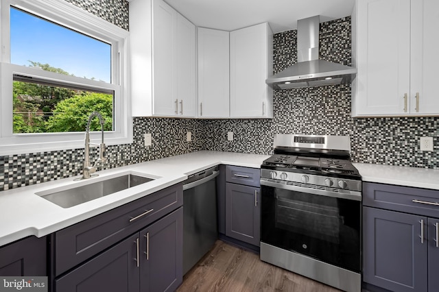 kitchen with wall chimney range hood, appliances with stainless steel finishes, a sink, and light countertops
