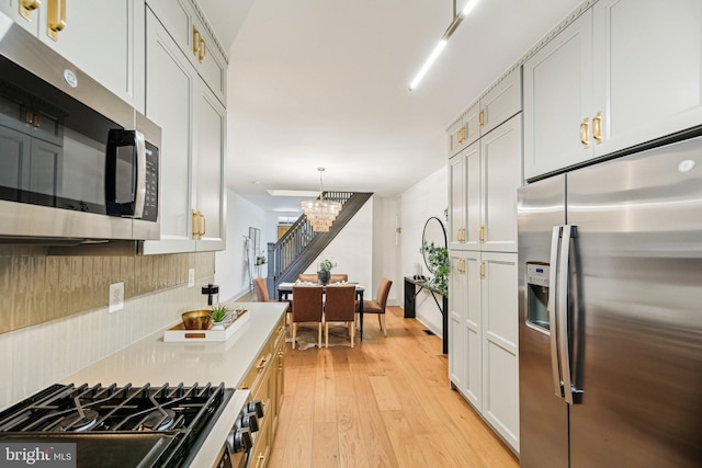 kitchen featuring stainless steel appliances, light wood-style floors, a chandelier, light countertops, and hanging light fixtures