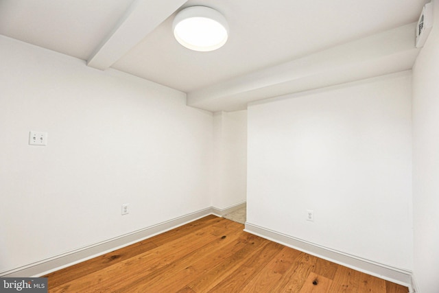 empty room featuring beamed ceiling and light wood-type flooring