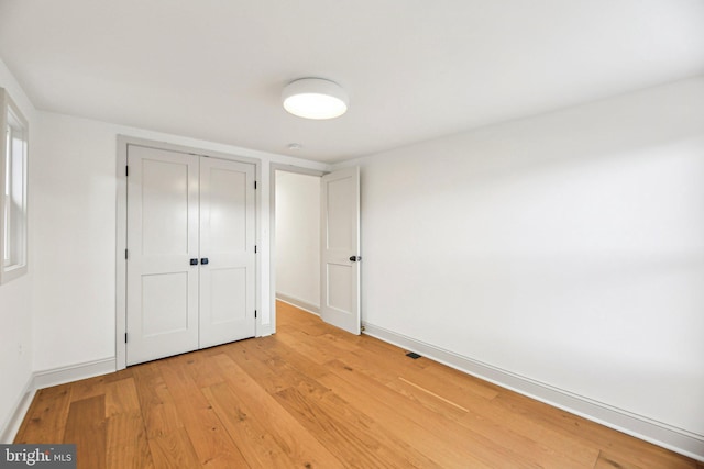 unfurnished bedroom with light wood-style flooring, a closet, and baseboards