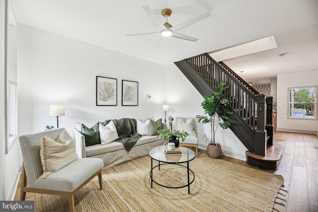 living area with stairway, wood-type flooring, baseboards, and a ceiling fan
