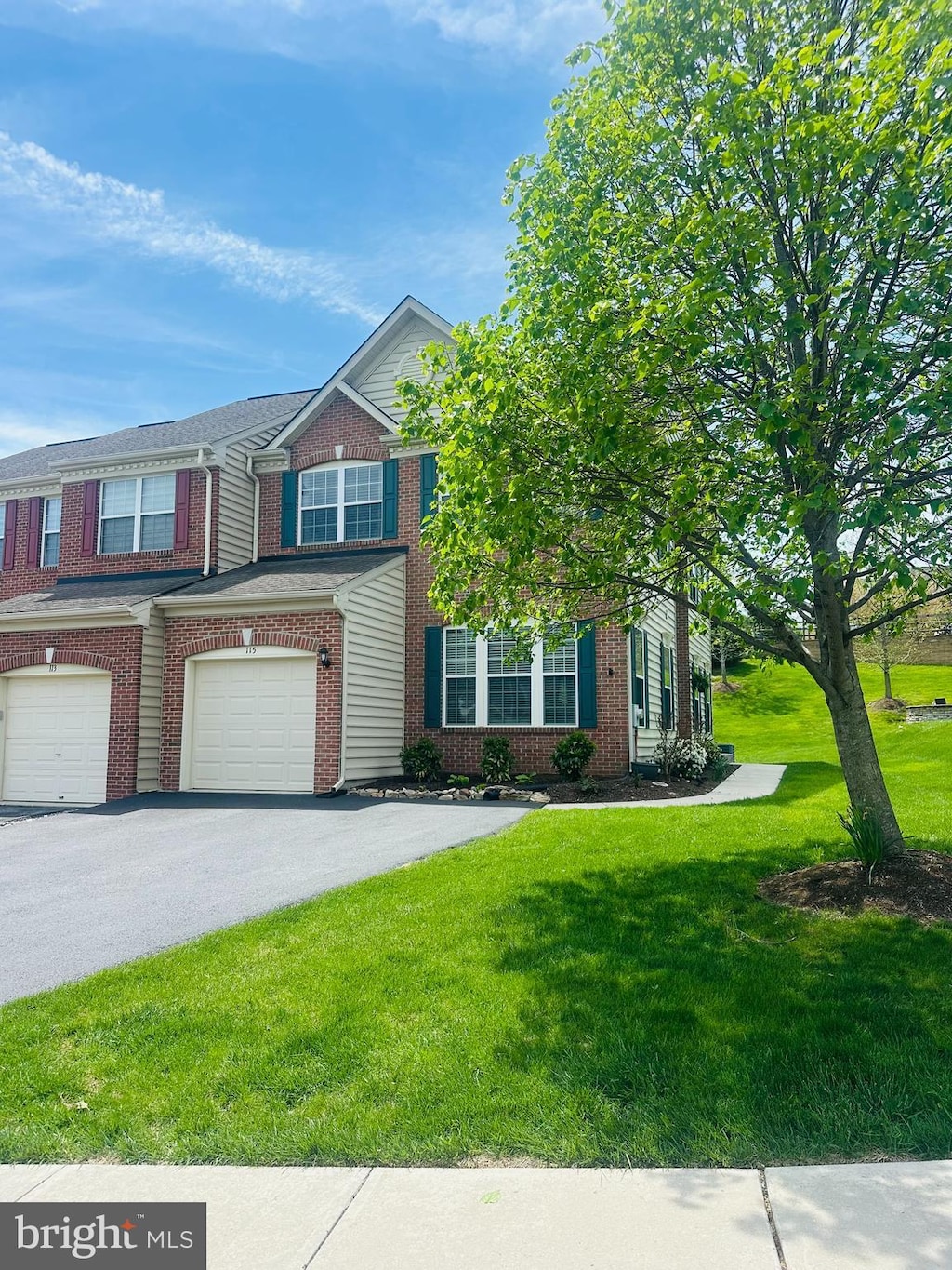 multi unit property featuring brick siding, an attached garage, driveway, and a front lawn