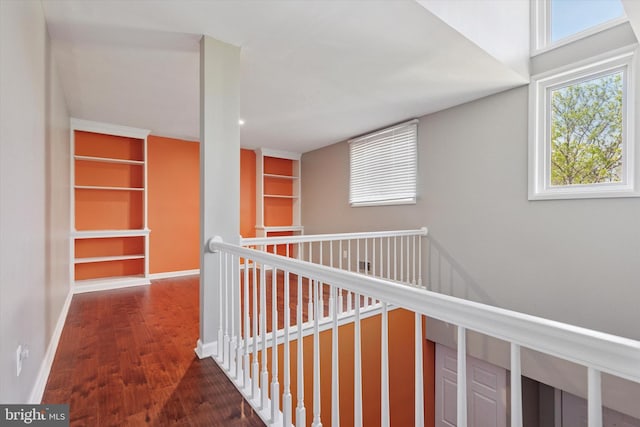hallway with baseboards, an upstairs landing, wood finished floors, and built in shelves