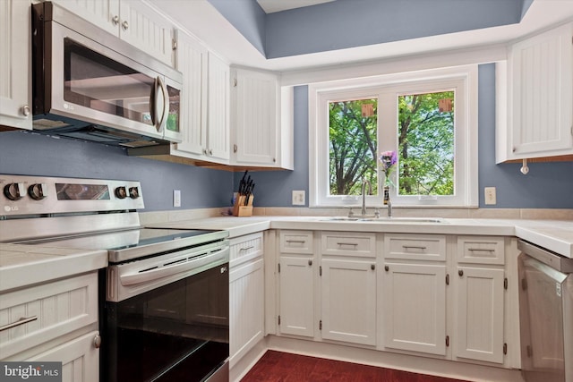 kitchen featuring white cabinets, dark wood-style flooring, appliances with stainless steel finishes, a sink, and light countertops