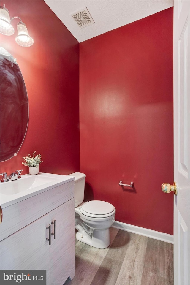 half bathroom featuring visible vents, wood finished floors, vanity, baseboards, and toilet