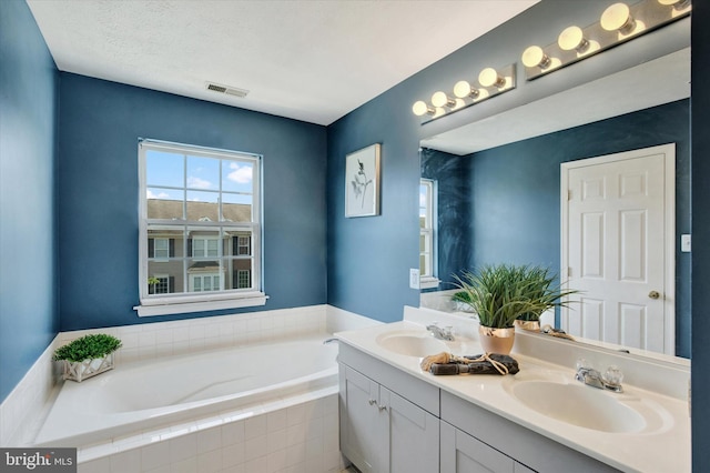 full bath with visible vents, a sink, a garden tub, and double vanity