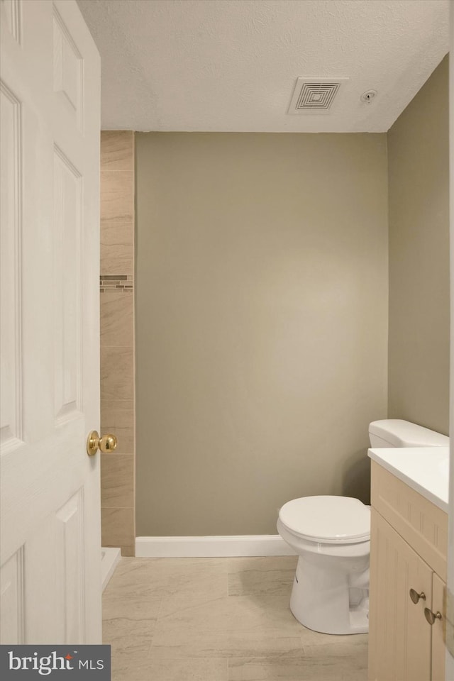 bathroom with vanity, toilet, a textured ceiling, baseboards, and visible vents