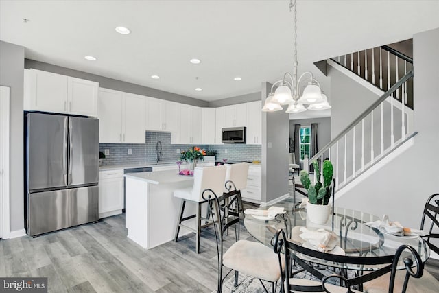 kitchen featuring decorative backsplash, appliances with stainless steel finishes, a center island, light countertops, and white cabinetry