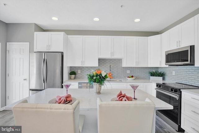 kitchen with white cabinets, a sink, light countertops, stainless steel appliances, and a kitchen island