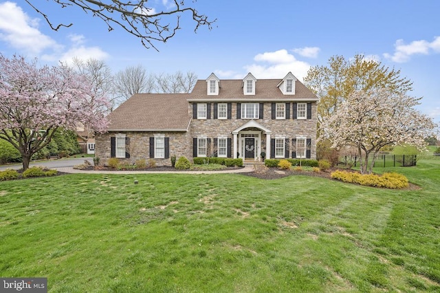 colonial home featuring fence, stone siding, and a front lawn