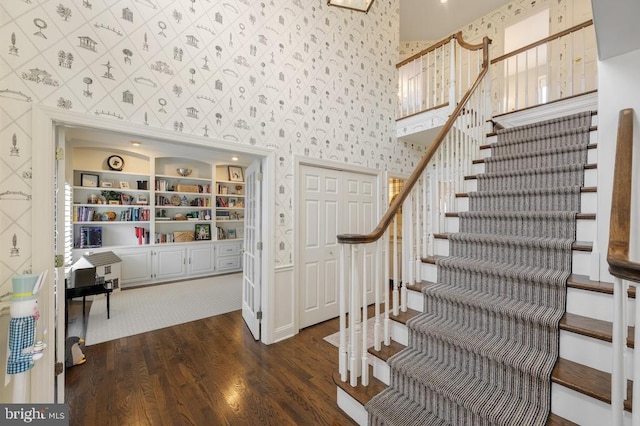 stairs featuring a towering ceiling, wood finished floors, and wallpapered walls